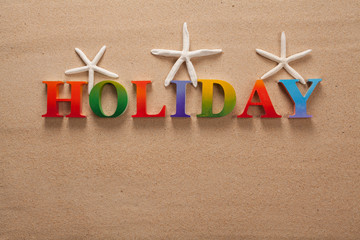 .holiday written in colorful letters decorate with shellfish on the beach with copy space