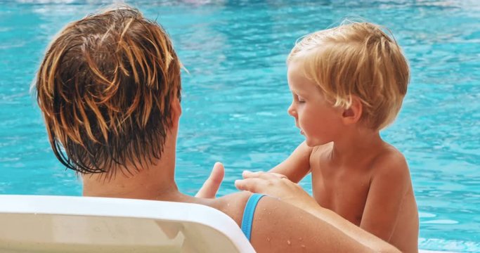 Mother and son relaxing at sunbed near pool at resort