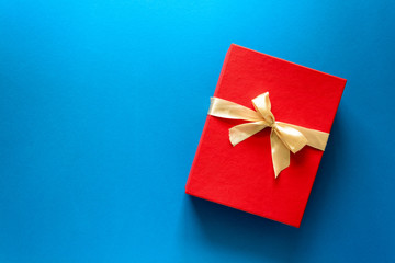 Top view on red Christmas gift box decorated with ribbon on blue paper background. New Year, holidays and celebration decorations concept. Copy space. Flat lay