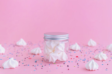 White meringues in glass jar on pink background