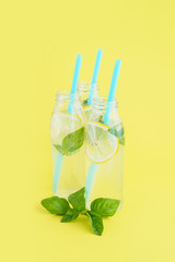 Lemonade in glass bottles with straws on bright yellow background