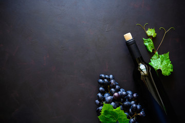 Bottle of red wine, grapes and leaves lying on dark wooden background. Top view. Flat lay. Copy space