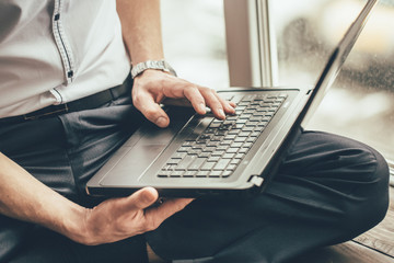 the laptop is in the hands of a man. He sits at the window with a clock on his hand and dials a message