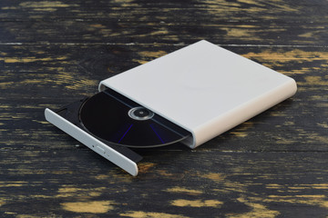 External CD/DVD/Blu-Ray Drive with opened tray and gray Blu-ray (BD) disc on dark brown background...