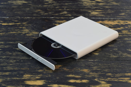 External CD/DVD/Blu-Ray Drive with opened tray and gray Blu-ray (BD) disc on dark brown background (right angle view)