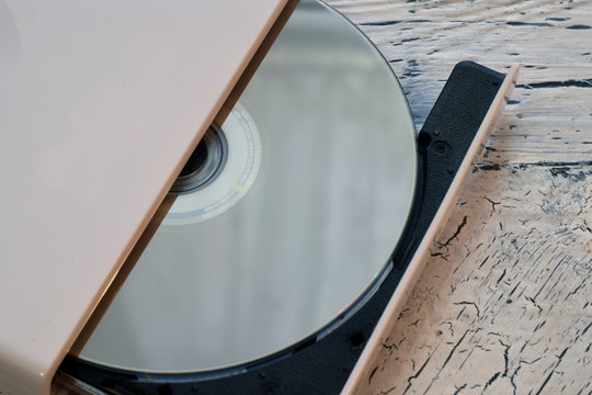 External CD/DVD/Blu-Ray Drive with opened tray and golden Blu-ray (BD) disc on white wooden background (left angle cropped view)