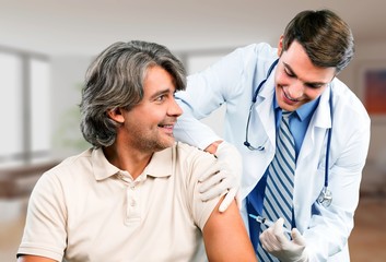 Obraz premium Handsome doctor making vaccination to male patient on background