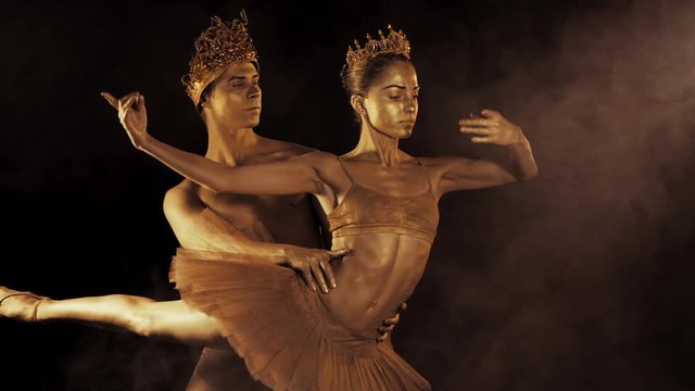 Professional, emotional ballet dancers with crowns on dark smoke scene performed by sexual couple king and queen with golden body art. Shining gold skin. Slow motion