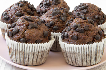 Chocolate cupcakes on pink plate on white wooden surface, side view. Close-up.