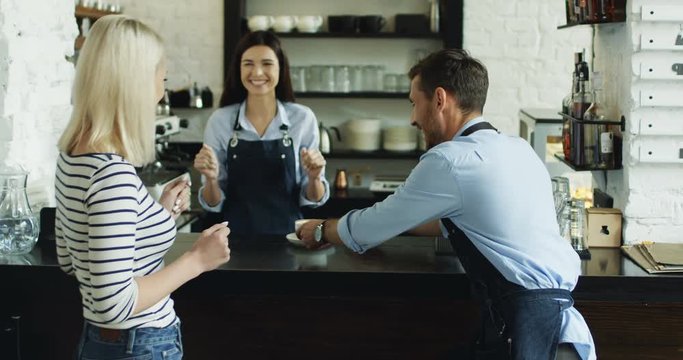 Joyful young waitress and waiter having fun and dancing while serving coffee to the beautiful woman at the bar.