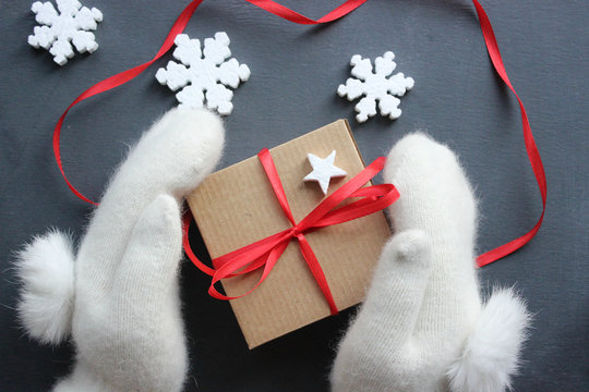 Christmas composition. Gift box with red satin ribbon holding hands in white fur mittens. Christmas decor. Extensive series of holiday pictures with various props and backgrounds. A lot of copyspace f