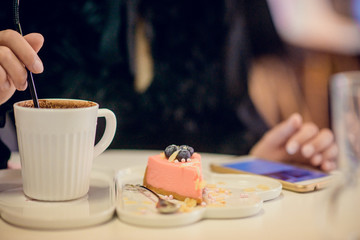 Women's hands with phone and pink cheesecake on a white dish-cloud, next to a mug of hot chocolate, the concept of a leisurely lunch in a cafe