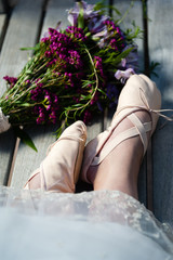 Woman's feet in ballet slippers with lace hem and a nearby bouquet of wildflowers.