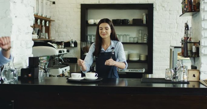 Cheerful Caucasian waitrees and waiter dancing and having fun while working at the bar. Woman making coffee and giving five to the man.