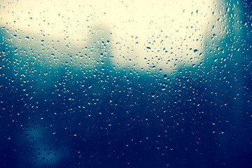 Raindrop on glass window, blue drops. City silhouette