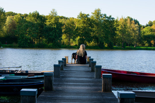 Junges Mädchen und ihr Hund sitzen gemeinsam auf einen Bootssteg und schauen einheitlich auf das Wasser. Standort: Deutschland, Nordrhein Westfalen