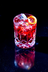 Red cocktail with ice, apparently, of Campari with red grapefruit on a black background.