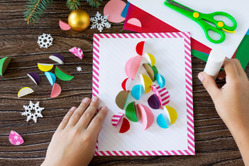 The child glues the parts Christmas tree greeting card. Handmade. Project of children's creativity, handicrafts, crafts for kids.