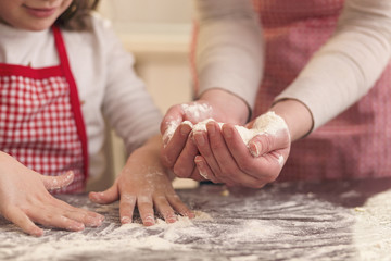 Obraz na płótnie Canvas Little girl sprinkling flour over the kitchen table for kneading dough