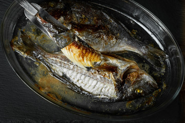 Baked sea fish with seasoning in baking pan on wooden table background.