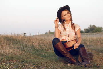 Girl cowgirl in jeans boots shirt and with a bag in a box with a wheel by a tree