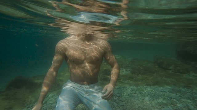 Young Attractive man comes out of the water in the sea. Male model on the shore. Slow motion, Underwater shooting
