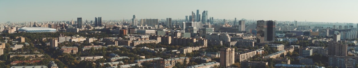 Obraz premium Panorama of evening summer cityscape with the residential district and dwelling houses in the foreground, multiple office skyscrapers and business high-rises in the distance; huge stadium on the left