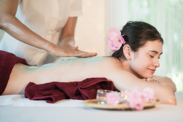 Obraz na płótnie Canvas Young Asian woman receiving salt massage in spa salon, Hand putting salt scrub on female back, Spa concept