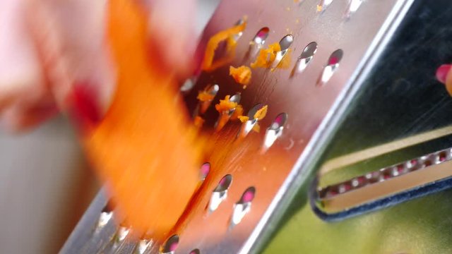 Close up of woman hand grating carrot on kitchen board in slow motion using vegetable grater