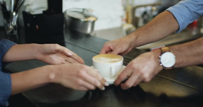 Close up of the male hands of waiter giving coffee to the female client. At the bar in the cafe.