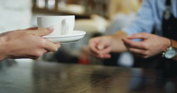 Hands of the Caucasian waiter passing cup of coffee to the female client. At the bar in the cafe.
