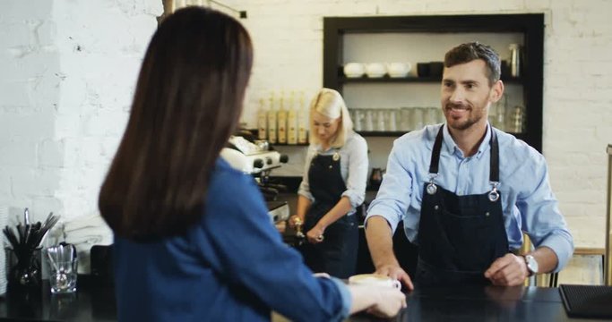 Rear of the brunette woman client sitting at the bar in the cafe and waiter giving her cup of coffee.