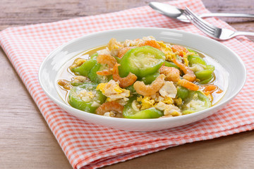stir fried luffa with egg and dried shrimp in a ceramic dish on wooden table. delicious and healthy homemade style food concept.