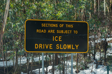 Winter road in Australian alps ice on road yellow lane marking Drive Slowly warning sign