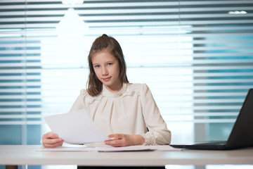 young girl businesswoman in casual clothes, sitting at a table closely look at documents, working at computer