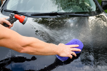 Close-up Of Hand With purple Brush Washing black Car.Car washing concept.man washing own car with sponge and soap.Copy space
