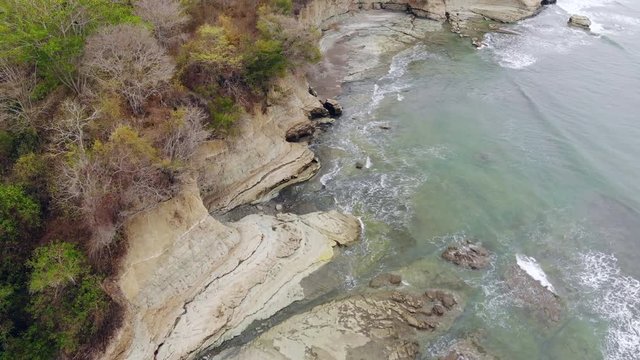 Aerial shot of an undeveloped tropical beach "Playa Escondida" in Esmeraldas province, Ecuador, with exposed mudstone pavement and cliffs, tropical dry forest growing on clifftops.