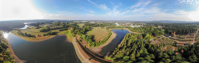 Artificial pond in the Harz Mountains with a neighbouring meadow and a small town in the background, aerial photo with the drone.