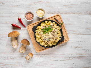 Pasta with penny bun on a cast iron pan on a white wooden table.
