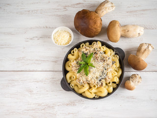 Pasta with penny bun on a cast iron pan on a white wooden table.
