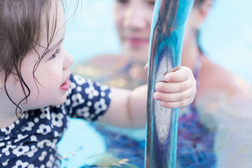 Summer holiday concept. Happy little girl playing in swimming pool with her mother