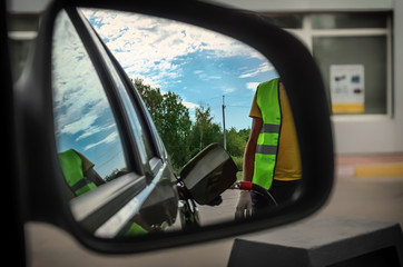 Fototapeta na wymiar Reflection in car mirror of the man fuel the car on petrol stati