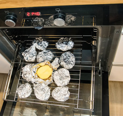 Halved potatoes wrapped in aluminum foil, lying on the grate of the oven.