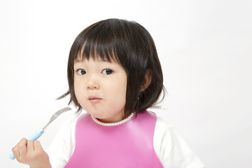 白バックでフォークを手に持ち食事中の幼い女の子、子供の健康、成長、食事,育児イメージ