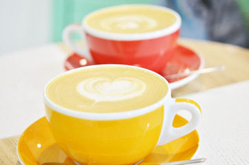 Two cup of coffee on a wooden table in a coffee shop. A cappuccino mug with a pattern on the foam.