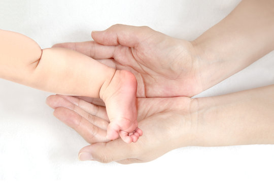 赤ちゃんの小さな片足を包むお母さんの大きな両手のアップ。成長と健康を喜ぶ母。母性、愛情、幸せ、育児、健康のイメージ