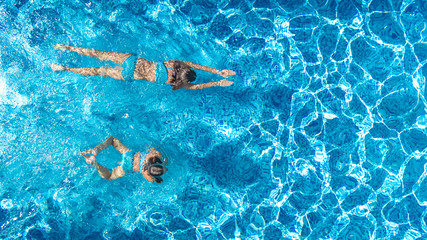 Aerial drone view of children in swimming pool from above, happy kids swim on inflatable ring donuts, girls have fun in water on family vacation
