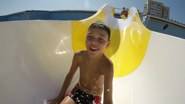 A funny view of a small boy in swim briefs sliding on a white and yellow aqua park tube. He is frightened a bit and moves down in slo-mo