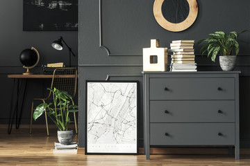 Poster between plant and grey cabinet with books in home office interior with lamp on desk. Real...