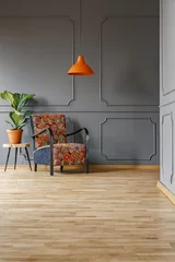 Fotobehang Boho Plant on a wooden side table and a comfortable armchair with a boho style pattern in a gray living room interior and copy space place for a floor lamp. Real photo.  © Photographee.eu